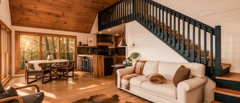 Amplia sala de estar con un sofá blanco, una escalera de madera y un comedor con mesa y sillas.