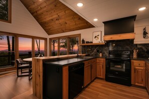 A modern kitchen with a wooden ceiling, large windows, and a view of the sunset. - Painted Sky Cabin - Long Distance Mountain Views! | Firepit | Pet Friendly (Morganton)