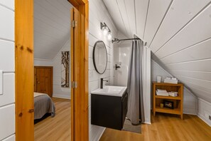 A bedroom with a bed, a bathroom with a sink and shower, and a wooden shelf with towels. - Painted Sky Cabin - Long Distance Mountain Views! | Firepit | Pet Friendly (Morganton)