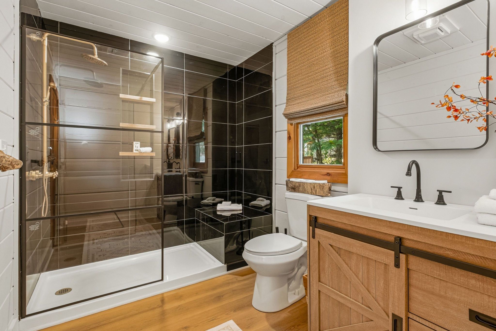 A modern bathroom with a glass-enclosed shower, a white toilet, and a wooden vanity with a mirror.