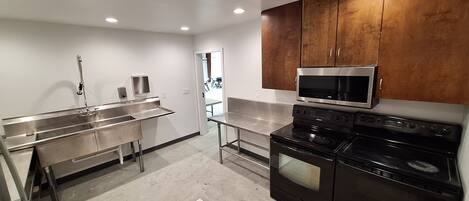 A modern kitchen with stainless steel appliances, wooden cabinets, and a visible door leading to another room.