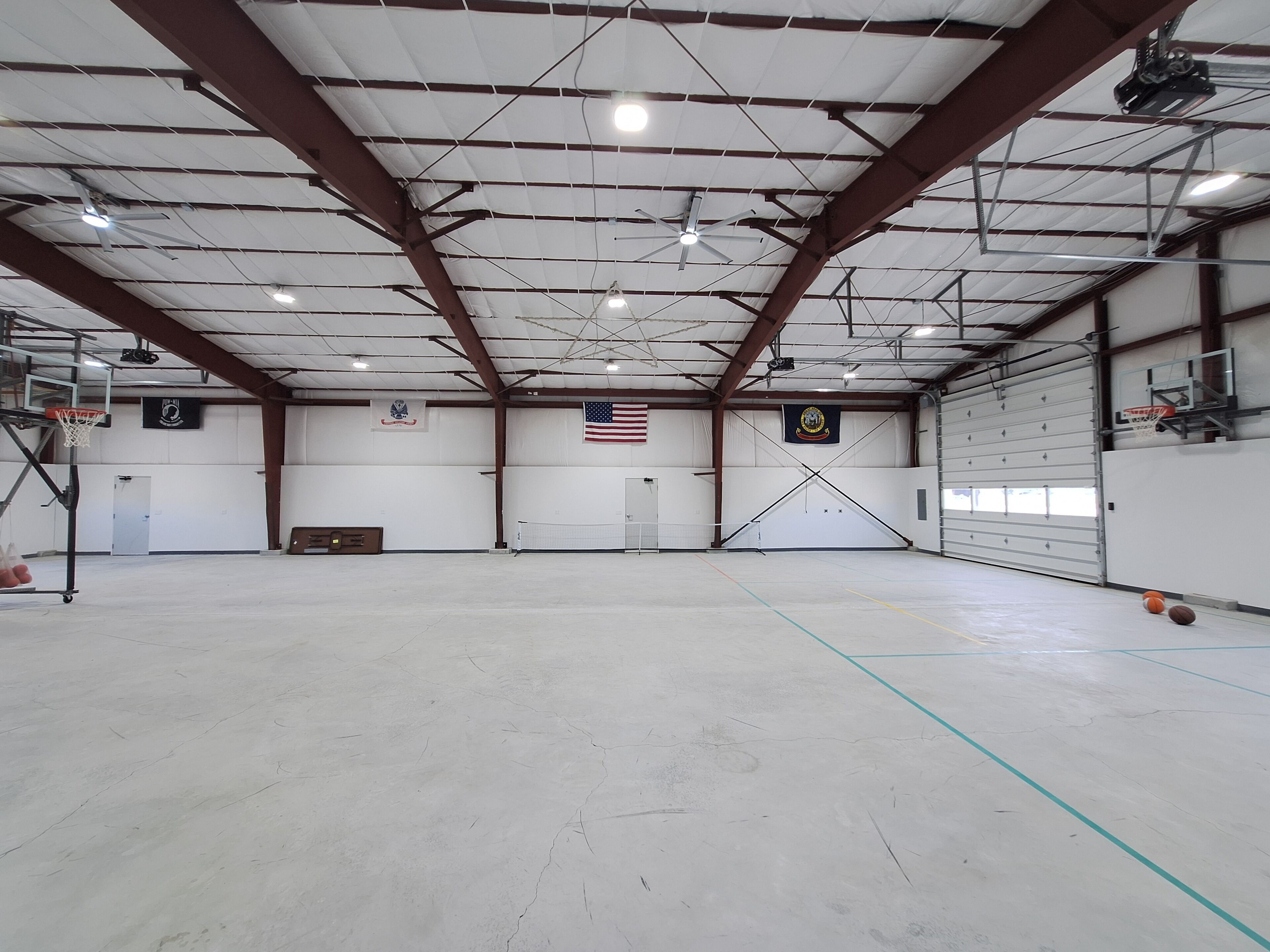 A large indoor space with a basketball court, ceiling fans, and a flag.