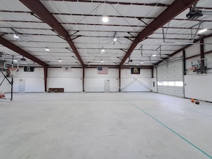 A large indoor space with a basketball court, ceiling fans, and a flag.
