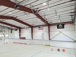An indoor sports facility with a basketball court, volleyball net, and a flag.