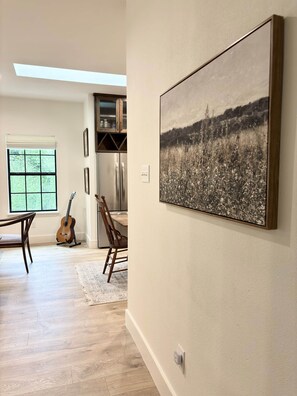 Una habitación con comedor, una guitarra, un cuadro y vistas a la vegetación por una ventana.