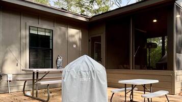 A covered barbecue grill, picnic tables, and a wooden deck in a residential setting.