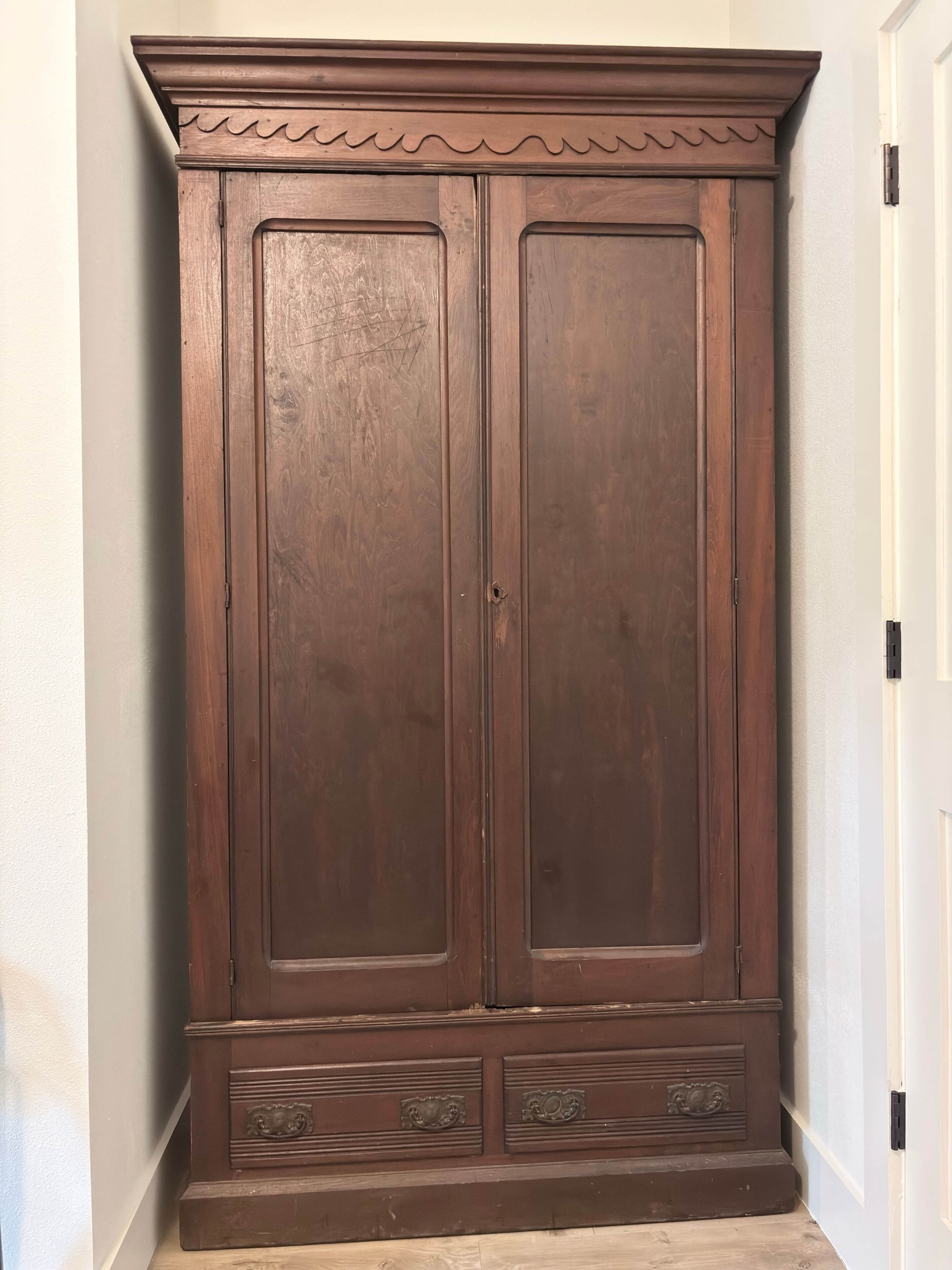 A large wooden wardrobe with two doors and a lower shelf.
