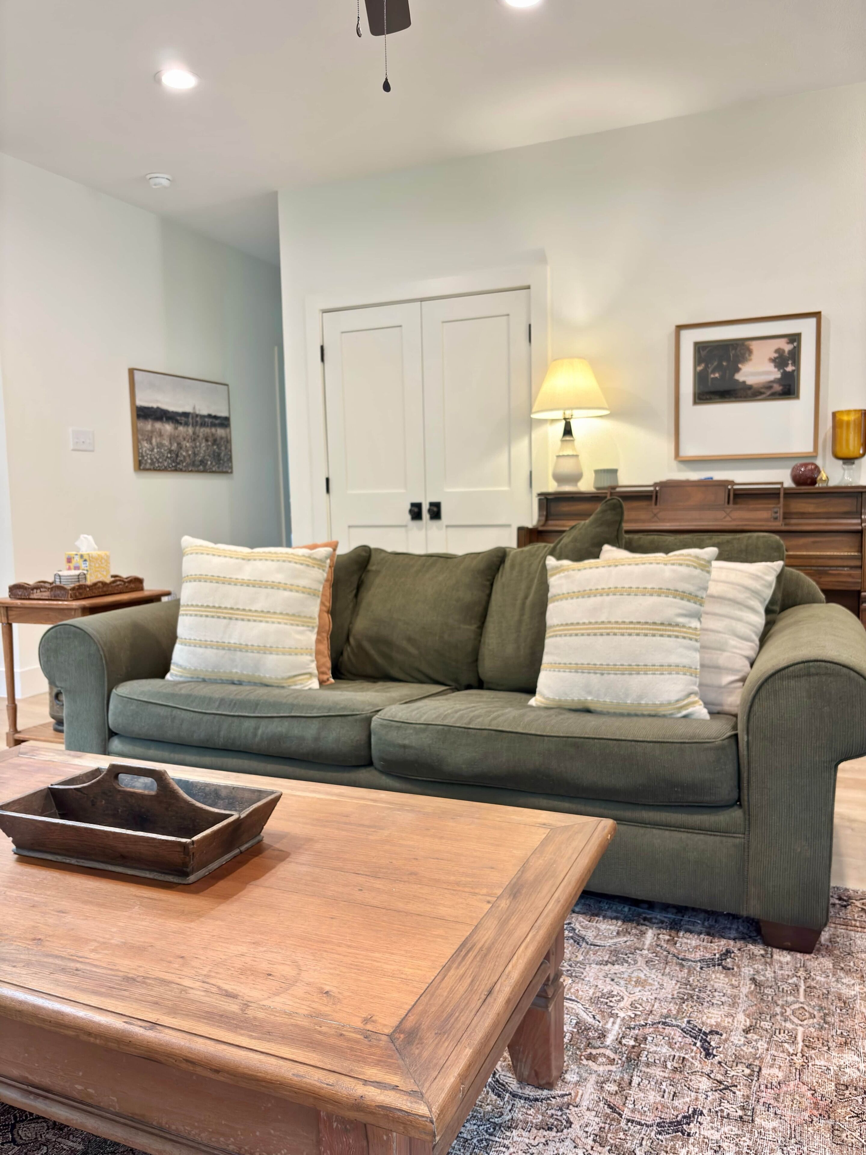 A living room with a green sofa, a wooden coffee table, a lamp, and a door in the background.