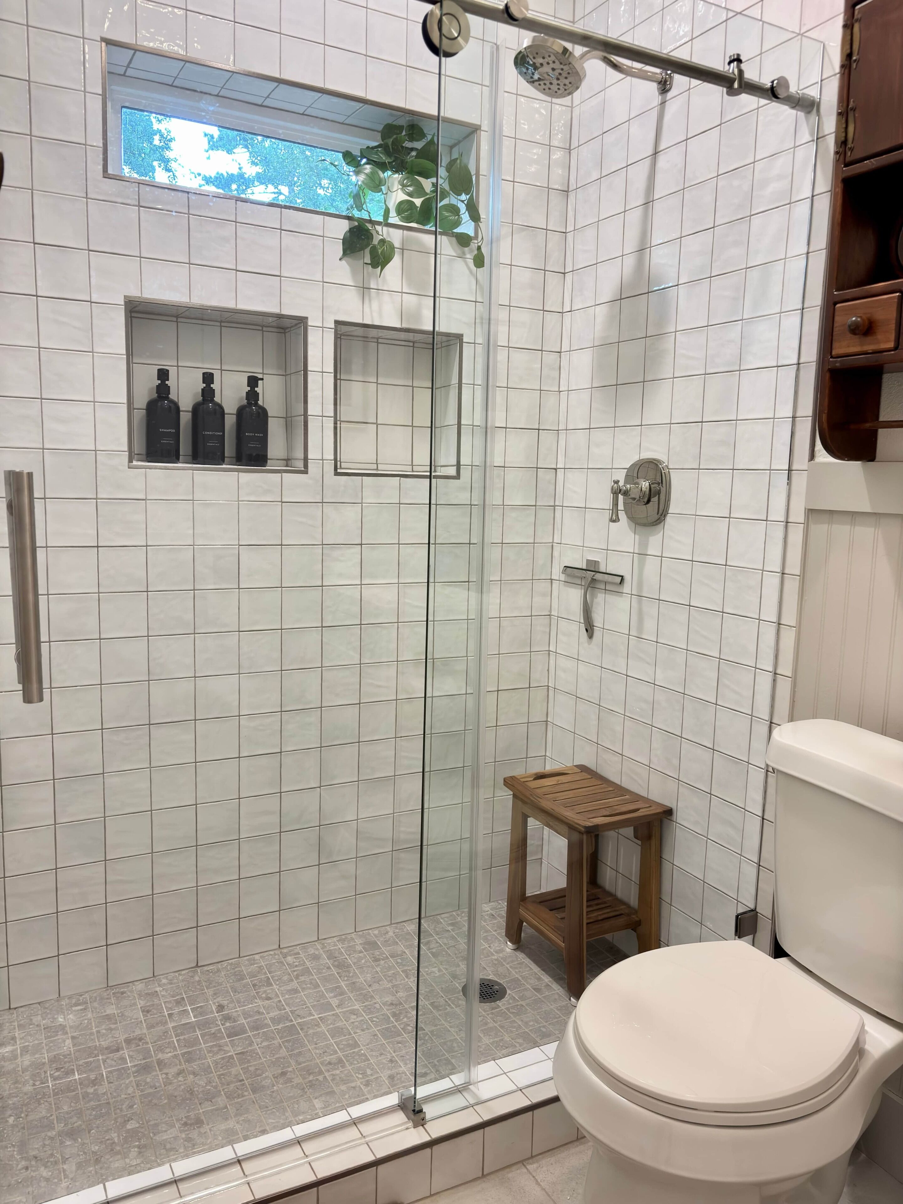 Une salle de bain avec une douche en verre, des toilettes et un petit tabouret en bois.