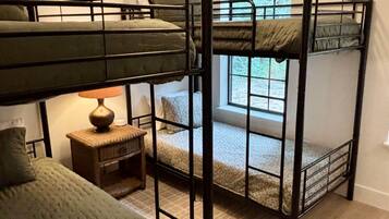 A bunk bed room with a ceiling fan, a small table with a lamp, and a window with a view.