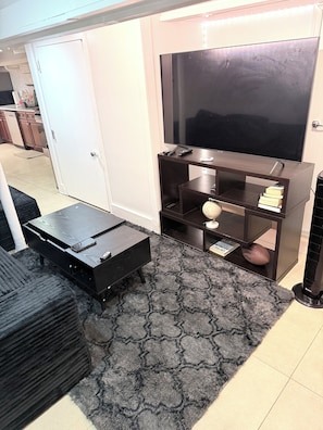 A living room with a flat-screen TV, a coffee table, a bookshelf, and a rug.