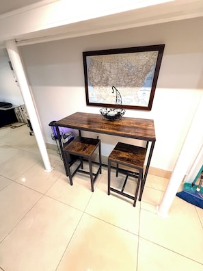A small dining area with a wooden table and two chairs, a framed map on the wall, and a white pillar.