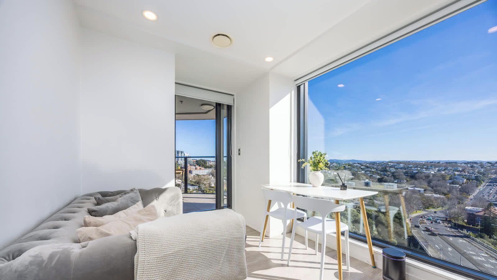 Ein modernes Wohnzimmer mit einer Couch, einem Esstisch mit Stühlen und einem großen Fenster mit Blick auf die Stadt.