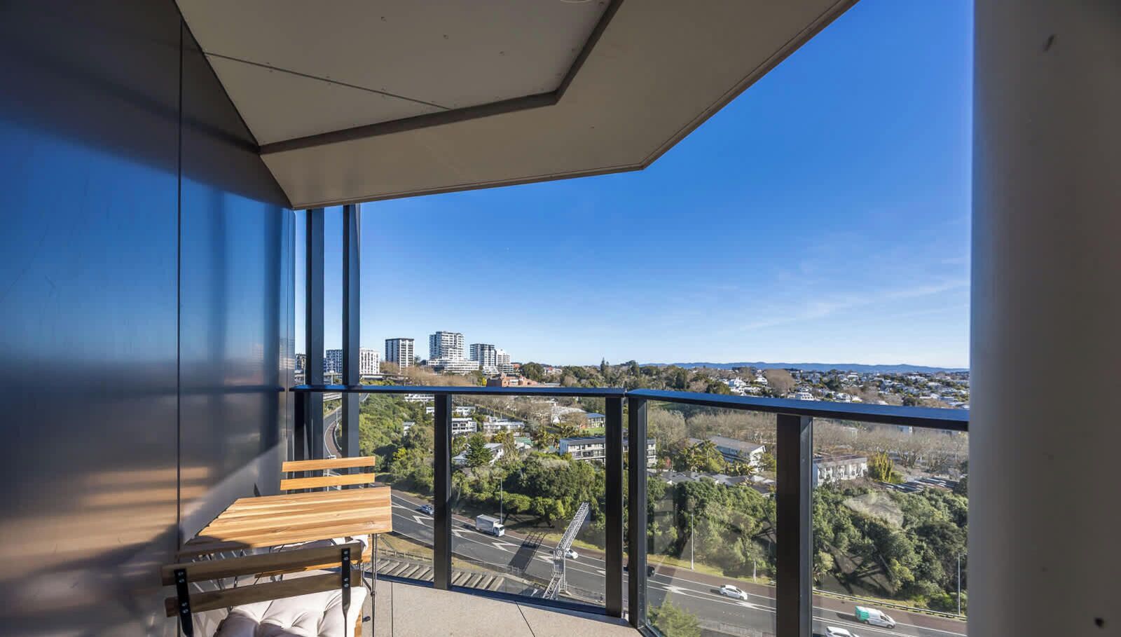 A balcony with a view of a cityscape, a wooden bench, and a clear sky.