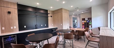 A modern kitchen with built-in appliances, a dining area with round tables and chairs, and a view of the city through a window.