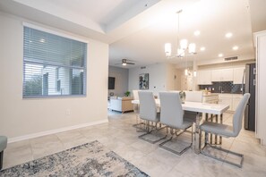 A modern kitchen with white cabinets, a black refrigerator, and a dining area with a white table and grey chairs. - 2BD Prime Location & Free Resort Access! (Kissimmee)