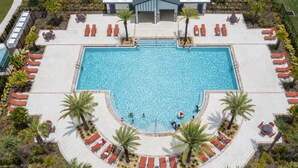 Une grande piscine rectangulaire entourée d’une terrasse aménagée, dotée de plusieurs chaises longues et d’un espace salon abrité.
