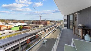 A high-rise building with a balcony overlooking a train station and industrial area.
