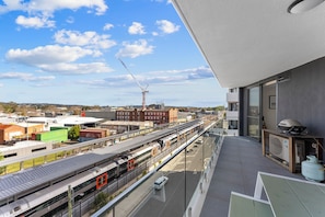 A high-rise building with a balcony overlooking a train station and industrial area.