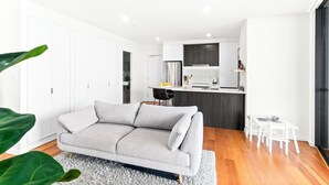 A modern living room with a sofa, a dining area with a table and chairs, and a kitchen with a refrigerator and cabinets.