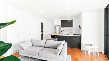 A modern living room with a sofa, a dining area with a table and chairs, and a kitchen with a refrigerator and cabinets.