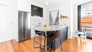 A modern kitchen with a stainless steel refrigerator, a round dining table with two chairs, and a large window with a view of shipping containers.