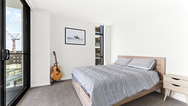 A bedroom with a bed, a guitar, a framed picture, and a view of a building through a window.
