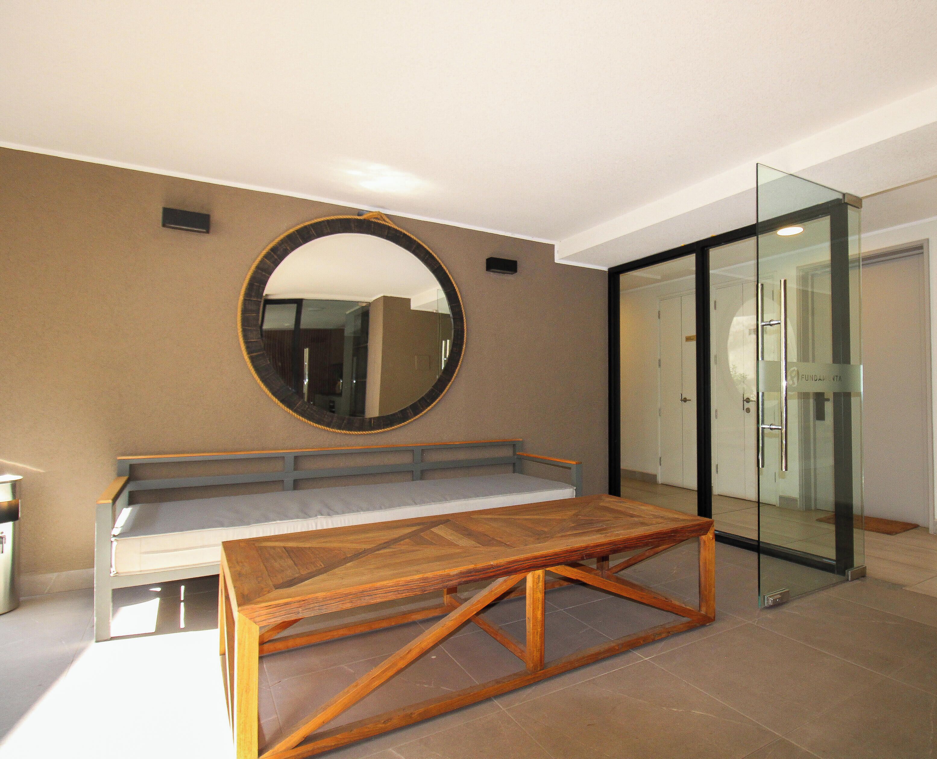 A room with a wooden bench, a round mirror, and a glass door.