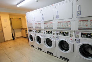 A laundry facility with multiple washing machines and dryers, each with QR codes and instructional labels. - Estudio Central Premium, WiFi, AC, heating (Santiago)
