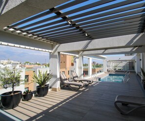 Eine Dachterrasse mit Pool, Liegestühlen und Topfpflanzen.