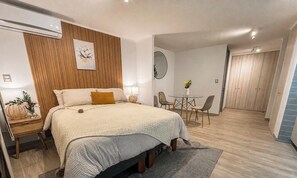 Habitación de hotel con cama, mesita de noche, lámpara y una pequeña zona de comedor con sillas y una mesa.