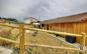 Edifici de fusta amb teulada de rajola, pati tancat amb plantes en testos i zona d'estar exterior coberta.