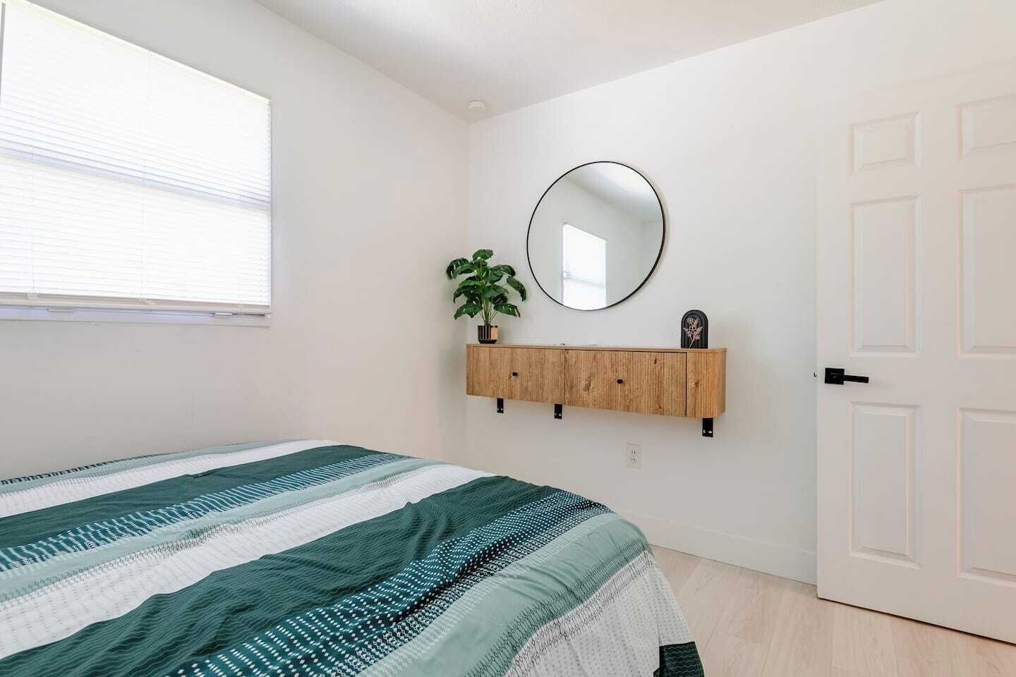 Ein Schlafzimmer mit einem Bett, einer Holzablage mit Spiegel, einer Topfpflanze und einer Tür.