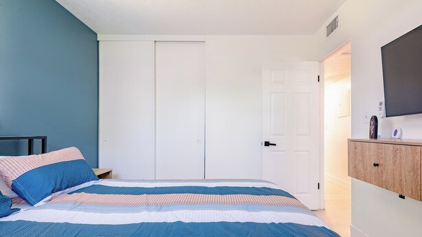 A bedroom with a bed, a wardrobe, a television on a wooden cabinet, and a door leading to another room. - Spacious Cocoa Retreat Near Beach & Port (Cocoa)