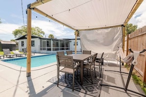 Ein Garten mit Pool, einer überdachten Terrasse mit Tisch und Stühlen sowie einer Hängematte.