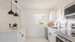 A modern kitchen with white cabinetry, a stainless steel range, and a window with blinds. - Spacious Cocoa Retreat Near Beach & Port (Cocoa)