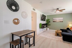 Una sala de estar moderna con comedor, un televisor de pantalla plana montado en la pared, un ventilador de techo y un cuadro en la pared.
