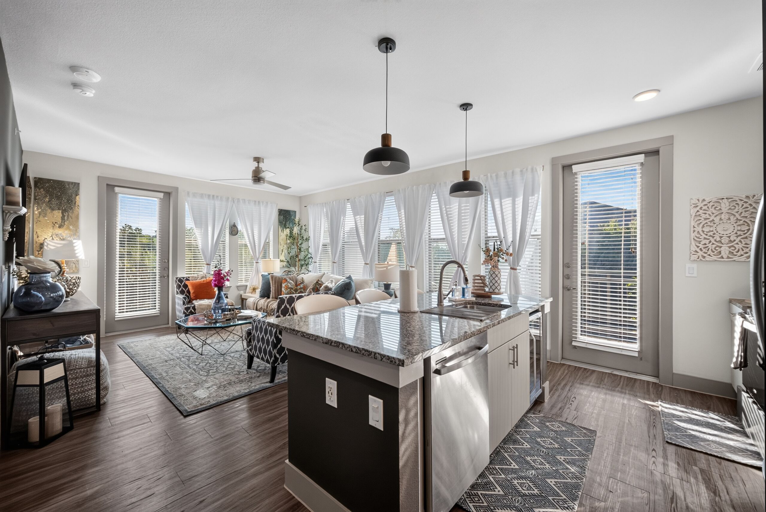 A modern kitchen with a central island, pendant lighting, and a dining area with a sofa and table.
