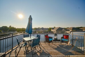 A wooden deck with a table and chairs, a blue umbrella, and a view of houses in the background. - The Bentley Collection - The Bentley Rooftop Residence (Dallas)