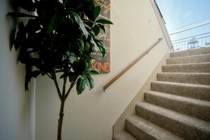 A carpeted staircase with a handrail, a wall-mounted sign with text, and a potted plant. - The Bentley Collection - The Bentley Rooftop Residence (Dallas)