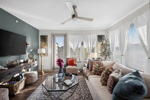 Ein Wohnzimmer mit Deckenventilator, Flachbildfernseher, einer Couch, einem Couchtisch und einem Fenster mit Jalousien.