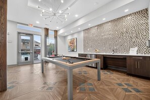 A modern indoor pool table with a geometric patterned floor, a contemporary light fixture, and a kitchen area with a patterned backsplash. - The Bentley Collection - The Bentley Rooftop Residence (Dallas)