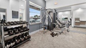 A gym with exercise equipment, a rack of dumbbells, and a window with a view of parked cars.
