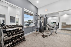 A gym with exercise equipment, a rack of dumbbells, and a window with a view of parked cars.