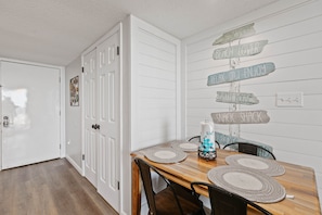 A dining area with a wooden table and chairs, a white door, and a wall with directional signs. - Stunning 2 BR Condo - Bring your Boat to the Beach - GSSR 709A (Gulf Shores)