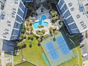 An aerial view of a modern building with a central swimming pool, tennis courts, and surrounding greenery. - Stunning 2 BR Condo - Bring your Boat to the Beach - GSSR 709A (Gulf Shores)