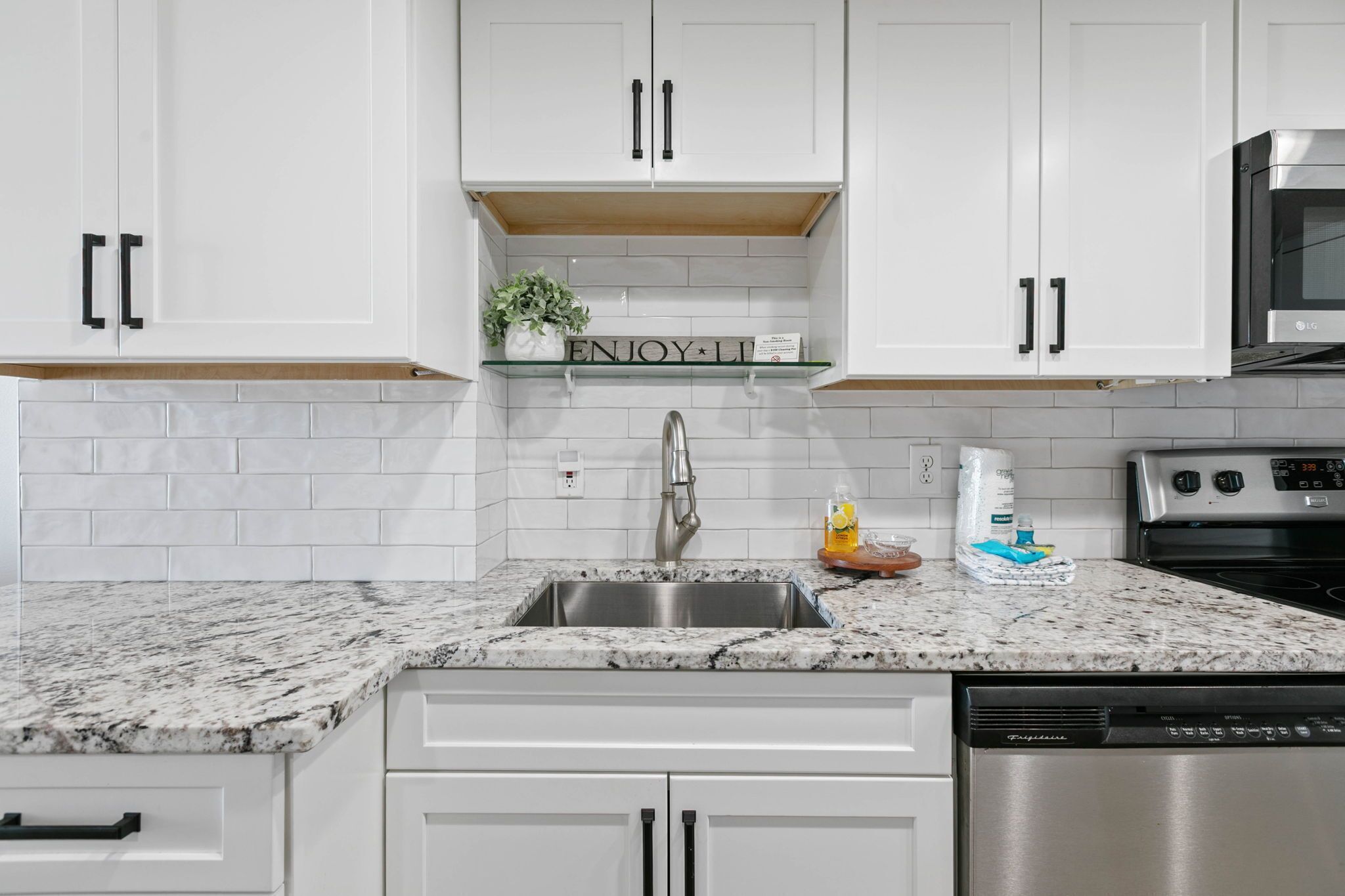 A modern kitchen with white cabinetry, a stainless steel sink, and a built-in microwave.