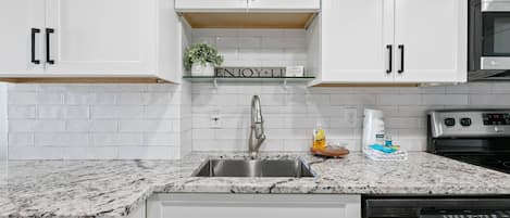 A modern kitchen with white cabinetry, a stainless steel sink, and a built-in microwave.