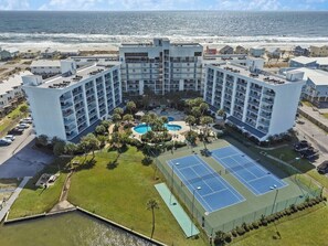 Ein mehrstöckiges Hotel mit Innenhof, Außenpool, Tennisplätzen und Blick auf den Strand.