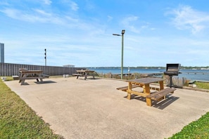 An outdoor patio area with picnic tables and a grill, overlooking a body of water. - Stunning 2 BR Condo - Bring your Boat to the Beach - GSSR 709A (Gulf Shores)